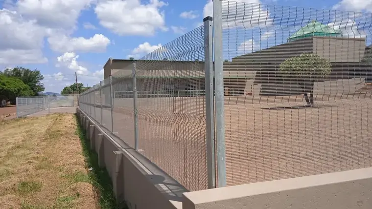 Silver mesh fence on a low concrete wall beside a paved building perimeter