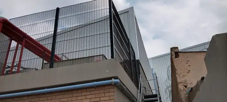 Mesh security enclosure on an elevated industrial platform beside pipework