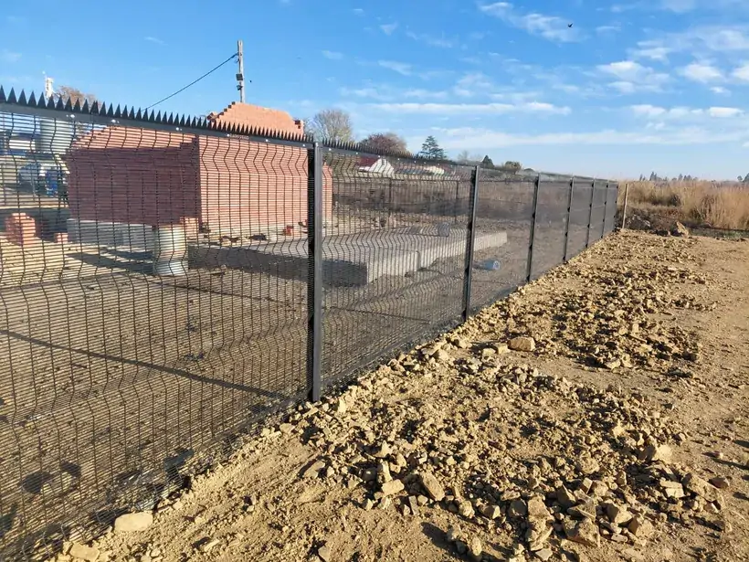 Dark spiked mesh panels along a trench near a brick building